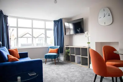 a living room with a blue couch and chairs and a clock at Wave Stays - First Floor Apartment - Heart of Cleveleys in Cleveleys