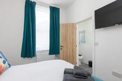 a bedroom with a bed with blue curtains and a toilet at Charles Alexander Short Stay - TheWestern Blackpool in Blackpool