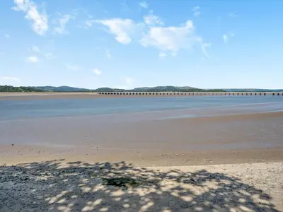 a beach with water and a bridge in the background at Mishmash in Arnside