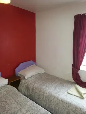 two beds in a room with red walls and a window at Jesmond International Hotel in Blackpool