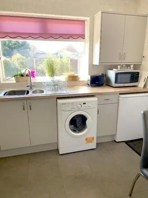 a kitchen with a washing machine and a microwave at Quiet secluded two bedroom bungalow with parking in Cleveleys