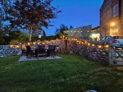 a table in a yard with a stone wall and lights at The Dairy at Brackenthwaite Farm in Carnforth