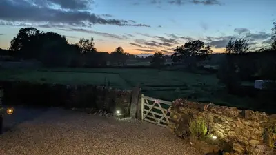 a sunset over a field with a stone fence at Corner Cottage at Brackenthwaite Farm in Carnforth