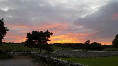a sunset over a stone wall in a field at The Coach House at Brackenthwaite Farm in Carnforth