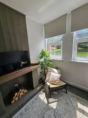 a living room with a fireplace and a chair and windows at Shakespeare's Snug in Prescot