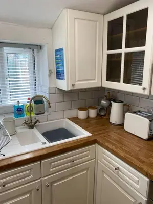a kitchen with white cabinets and a sink at 1750's cottage with open fire and beams in Upholland
