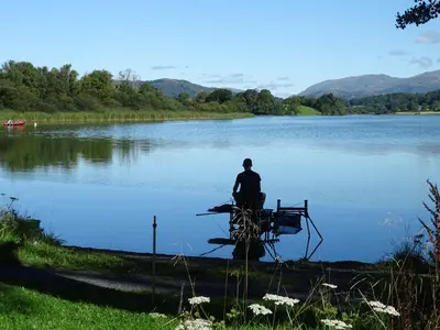 a person sitting on a picnic table in front of a lake at Kents Bank Holiday - Pet Friendly with Bay Views in Grange Over Sands