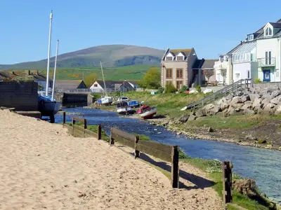 a beach next to a river with houses and boats at Cockleshell Cottage in Millom