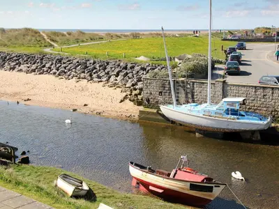 two boats are docked in the water near a road at Cockleshell Cottage in Millom