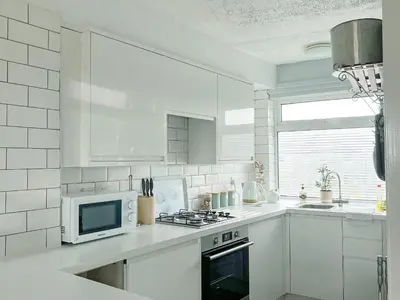 a white kitchen with a microwave and a stove at Cockleshell Cottage in Millom