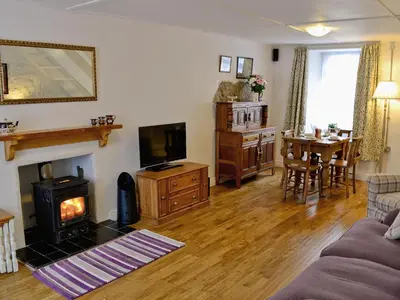 a living room with a fireplace and a tv and a table at Jackdaw Cottage in Baycliff