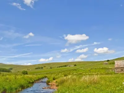 a river in the middle of a field with green hills at Jackdaw Cottage in Baycliff