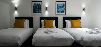 a room with three beds with yellow pillows at Temple Court by UStay Aparthotels in Liverpool