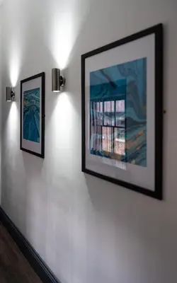 two framed paintings on a white wall with lights at Temple Court by UStay Aparthotels in Liverpool