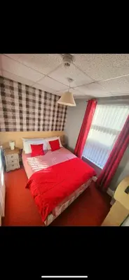 a bedroom with a bed with red sheets and a window at The Montclair in Blackpool