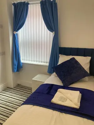 a bedroom with a bed with blue curtains and a window at The New Astoria Hotel in Blackpool
