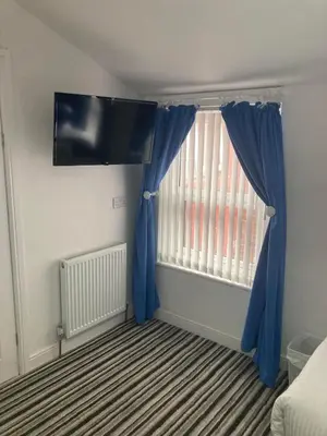 a bedroom with a window with blue curtains at The New Astoria Hotel in Blackpool