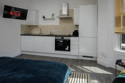 a kitchen with white cabinets and a bed in a room at Seaside Suite 1 - Great Location Perfect For Long Stays in Blackpool