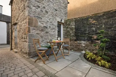 a patio with a table and chairs next to a stone wall at Wharton House Mews in Cartmel, Lake District - Ridgestone in Cartmel