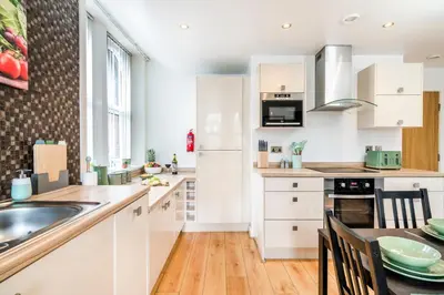 a kitchen with white cabinets and a table with chairs at Cavern Quarters, Beautiful Two Bedroom City Centre Apartment by Garudy Serviced Apartments in Liverpool