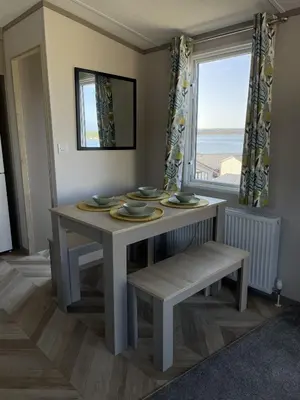 a dining room table and bench with a window at Lake View 92 in Millom
