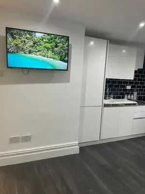 a white kitchen with a flat screen tv on a wall at Ground Floor Apartment 2, Lynton Apartments in Blackpool