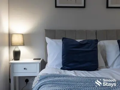 a bed with a blue pillow and a lamp on a night stand at Modern 2 Bed Apartment By Smooth Stays Short Lets & Serviced Accommodation Preston With Parking Near Train Station in Preston