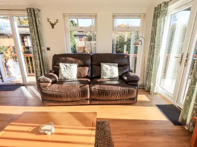 a brown leather couch in a living room with windows at Pippin Lodge in Grange Over Sands