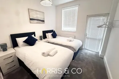 two beds in a bedroom with two windows at New Sandpiper Apartments in Fleetwood