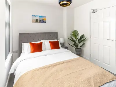 a white bedroom with a large bed with orange pillows at No10 Apartments in Blackpool