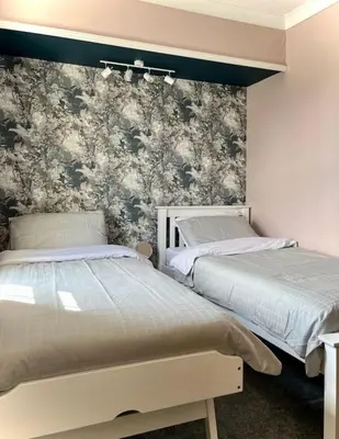 a bedroom with two beds and a wall with floral wallpaper at The Lytham Cottage in Lytham St Annes
