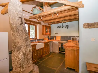 a kitchen with wooden cabinets and a large stone pillar at Egg Pudding Stone in Grange Over Sands