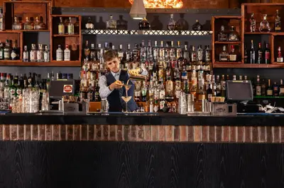a bartender standing behind a bar with bottles of alcohol at Titanic Hotel Liverpool in Liverpool