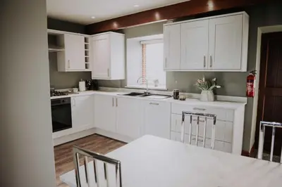 a kitchen with white cabinets and a table and chairs at Pattys Barn Holiday Cottages, Cabins and Venue Hire in Cockerham
