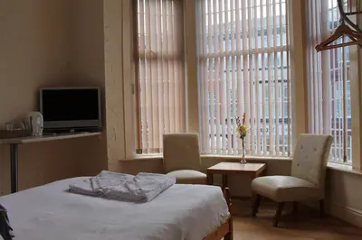 a bedroom with a bed and a tv and windows at Brecks Hotel in Blackpool