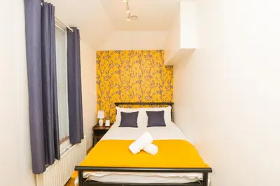 a small bedroom with a bed with a yellow headboard at Luxe Retreat - Steps from Stadium - Pool Table, Ping Pong, Football Table in Liverpool