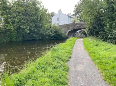 a path next to a river with a bridge at A modern, dog-friendly 3 bedrm canal side property in Bolton le Sands