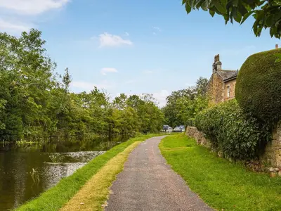 a dirt road next to a river with a building at Kiln Cottage in Bolton le Sands