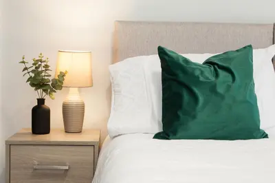 a bed with a green pillow and a lamp on a night stand at 8 Karslake Road in Wallasey