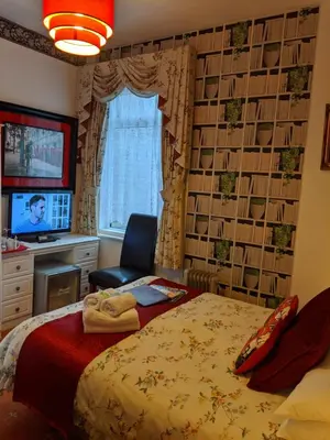 a bedroom with a bed and a chair and a television at The New Guilderoy Hotel in Blackpool
