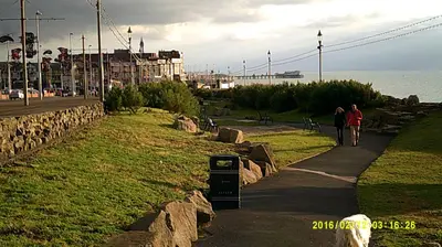 two people walking down a sidewalk next to the ocean at OLIVERS Strickley over 35 years only in Blackpool