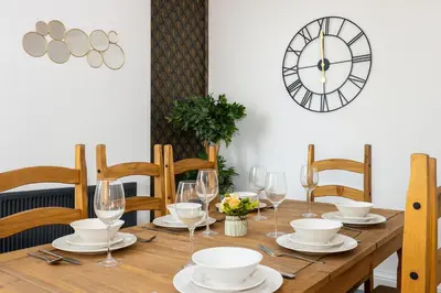 a wooden table with glasses and a clock on the wall at Spacious & Stylish 5 Bed with Free Street Parking in Morecambe