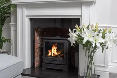a fireplace with a fire in a living room with flowers at Riversleigh in Warton