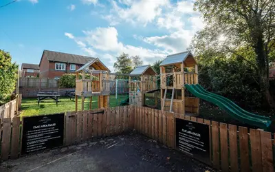 a wooden fence with a playground with a slide at Ye Olde Original Withy Trees in Bamber Bridge