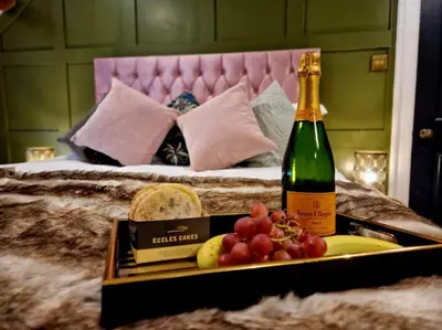 a tray with a bottle of champagne and grapes on a bed at Hamilton-The Cruck Luxury Let in Scorton