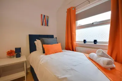 a bedroom with a bed with orange curtains and a window at Beautiful Stylish 2BD Flat - Free Parking 30 Percent Off Long term bookings in Wallasey