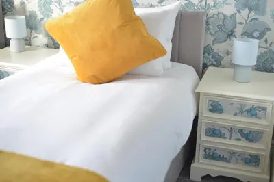 a white bed with a yellow pillow and a night stand at Huntsfield House- Stunning Modern 4 Bedroom House Suitable for Work and Leisure Stays in Bamber Bridge