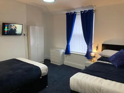 a bedroom with two beds with blue curtains and a tv at AGAPI APARTMENT - SEA VIEW SLEEPS TEN in Blackpool