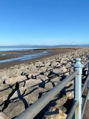 a fence on a beach with rocks and water at Eden Stay 5 Bedroom House in Morecambe