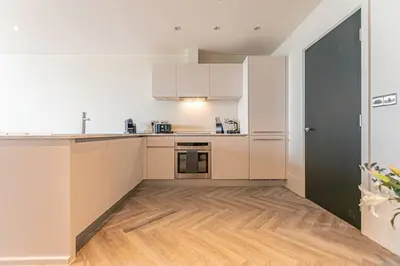 a kitchen with white cabinets and a wooden floor at 1BR Apt - Balcony - River View in Liverpool